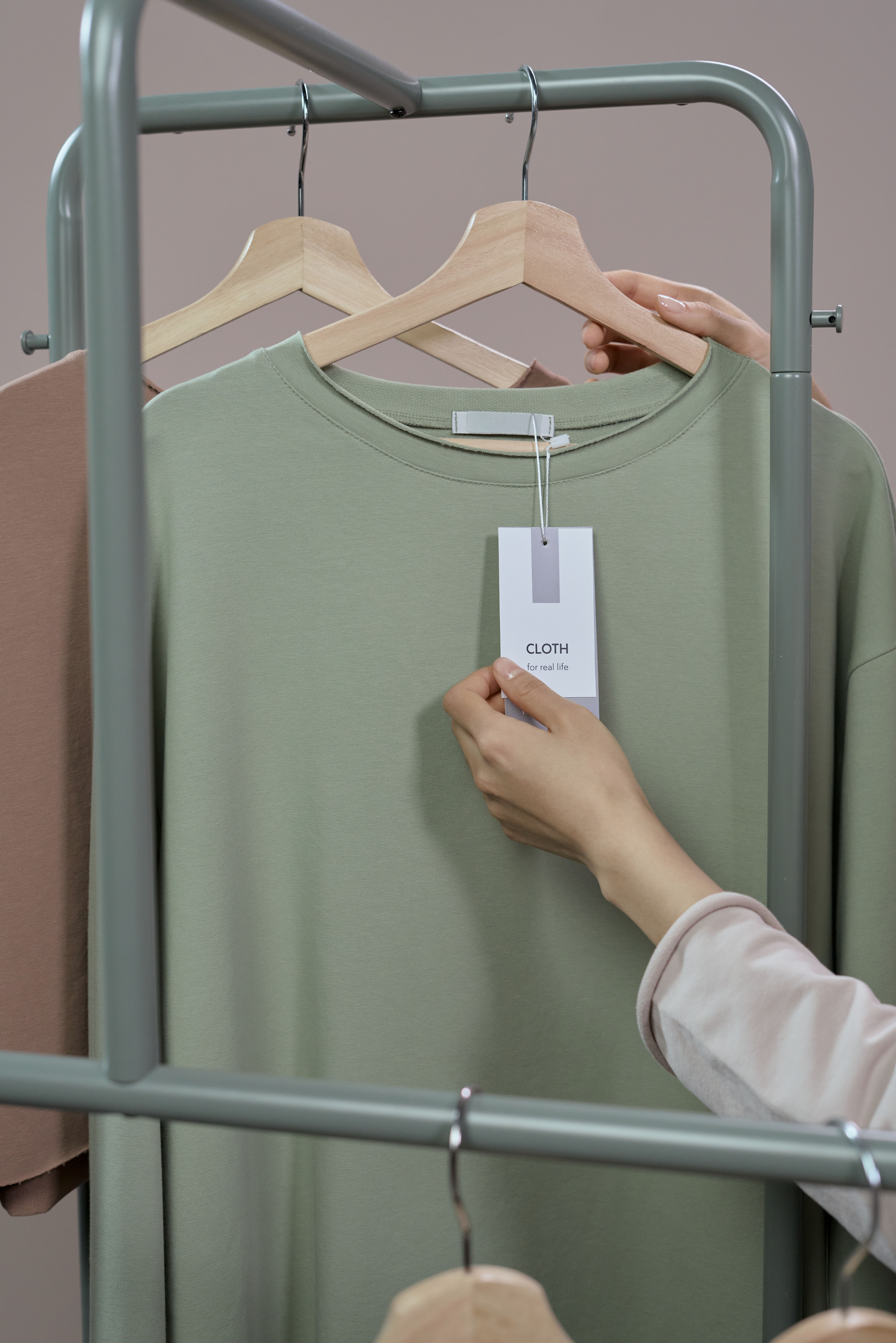 Hand bringt ein Preisetikett an einem T-Shirt an der Kleiderstange an